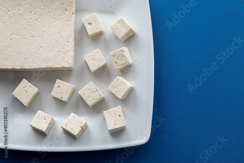 Tofu cut in cubes. Firm tofu on white plate. Vegan protein food.