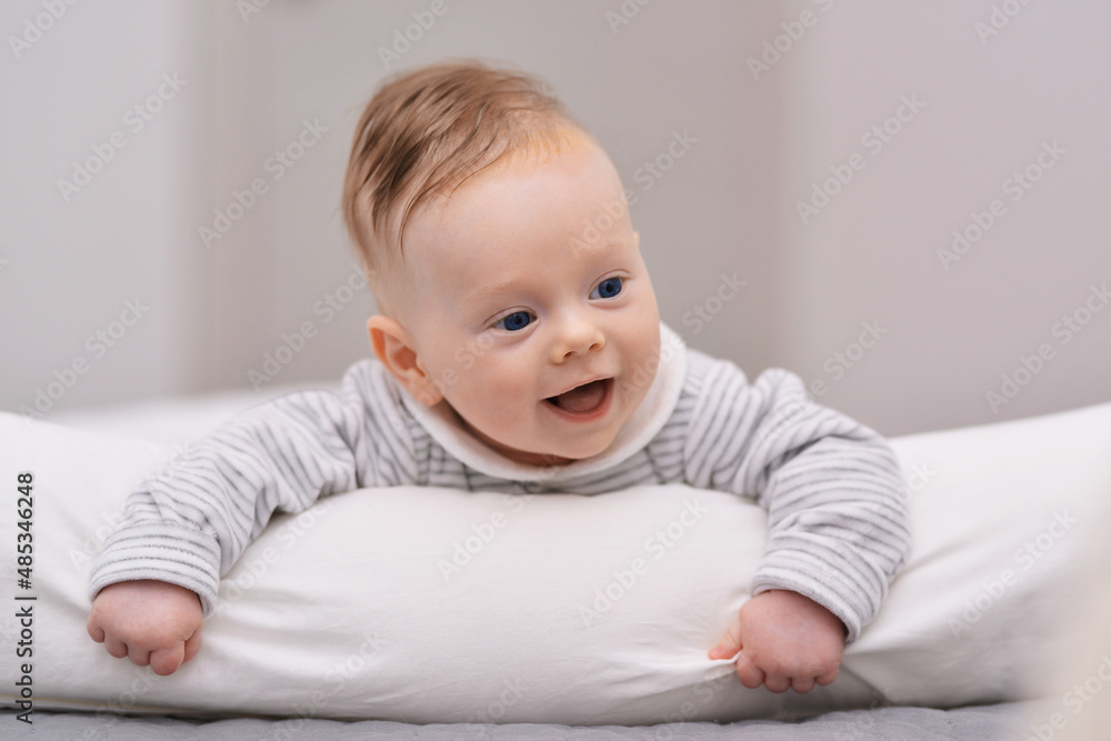 Adorable baby boy in white sunny bedroom. Newborn child relaxing on a bed. Nursery for young children. Furniture, textile and bedding for kids. New born kid during tummy time with toys.