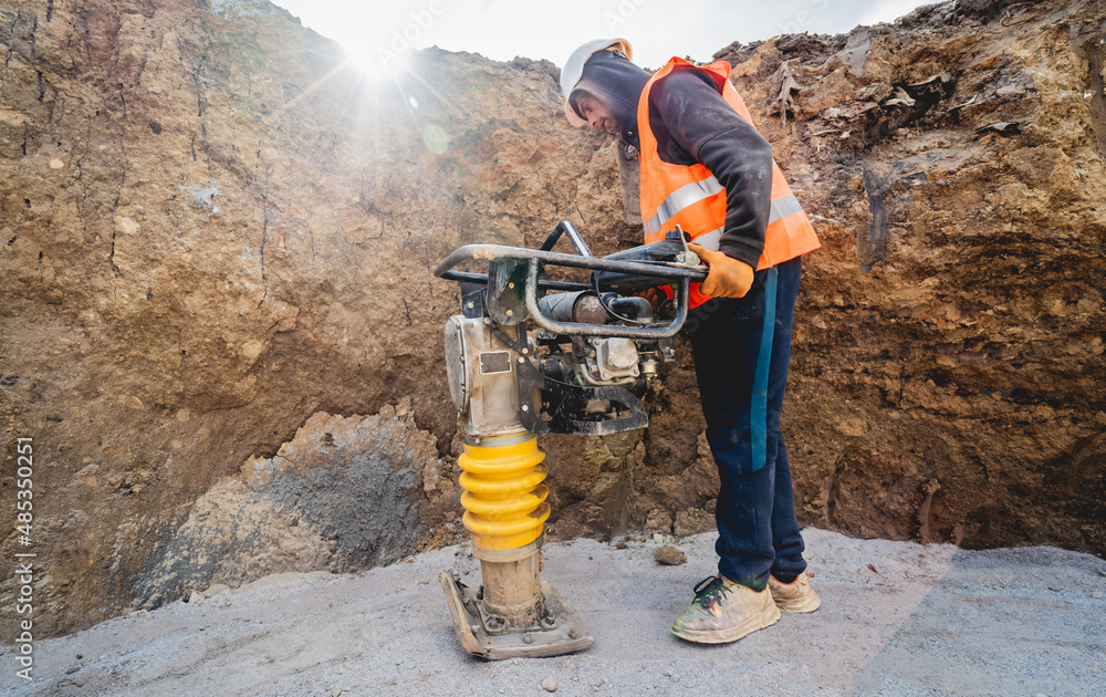 Worker uses a portable vibration rammer at construction of a power transmission substation Worker uses a portable vibration rammer at construction of a power transmission substation