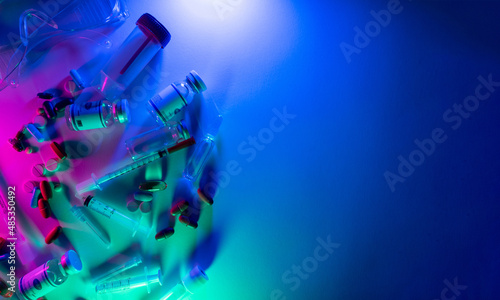 Medication background. Covid-19 drug. Pharmaceutical chemistry. Neon light vaccine injection dose bottle syringe pills lab goggles on bright pink blue green colorful copy space.