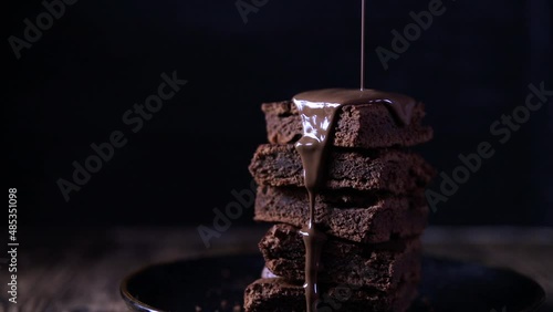 Brownie on a plate on a dark background, close up. Melted chocolate pours on cake pieces 