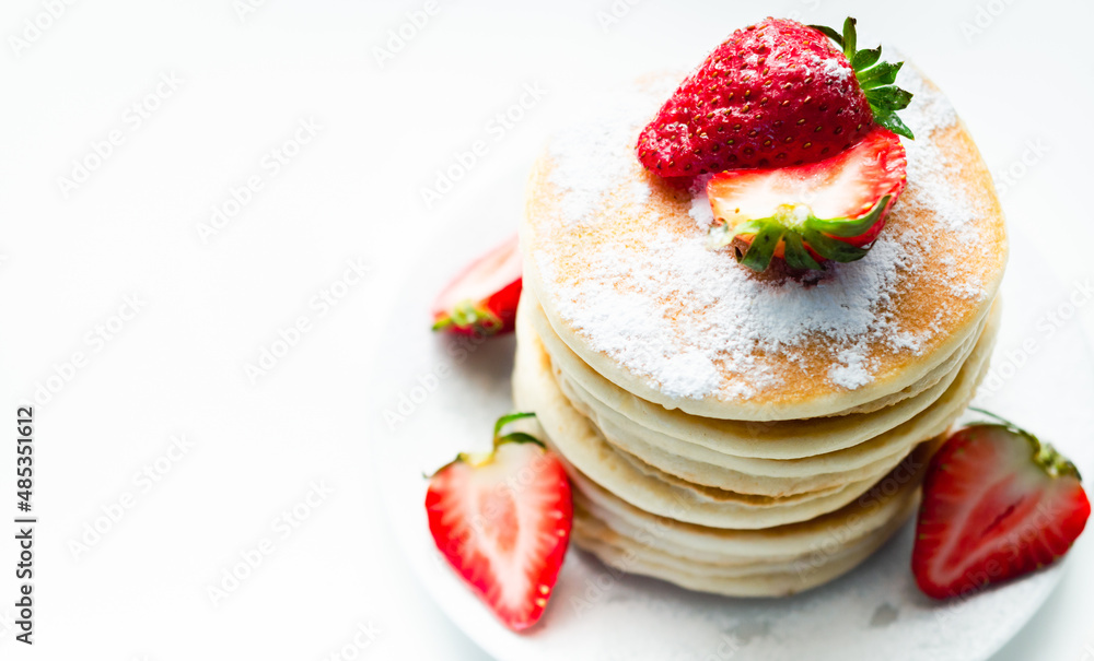 Delicious pancakes stacked with fresh sweet strawberries sprinkled with powdered sugar