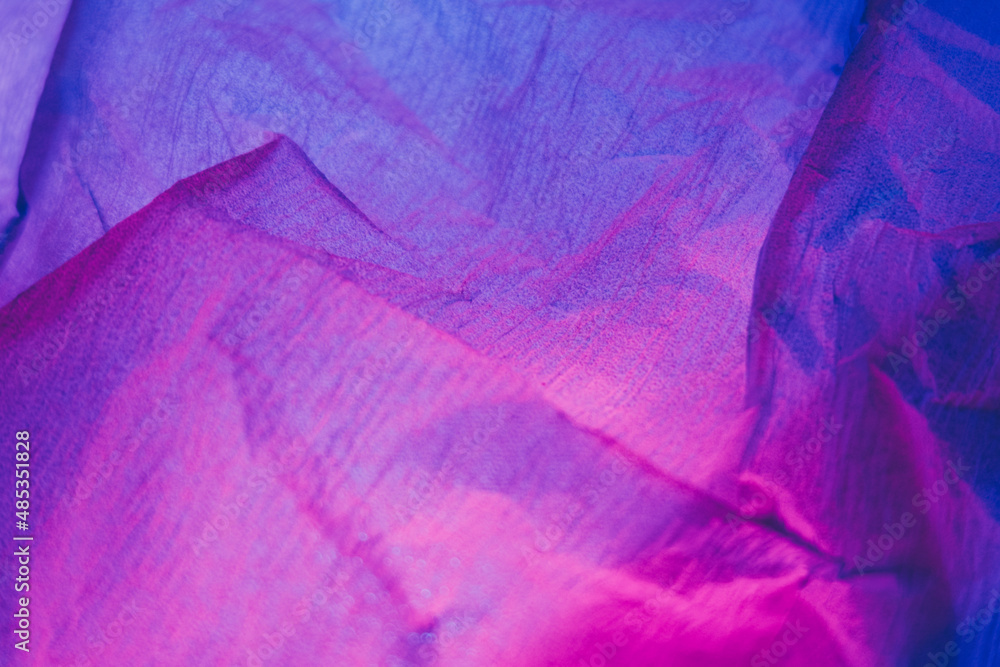 Creased paper texture. Ultraviolet background. Crushed material. Neon iridescent pink purple blue color gradient light grain noise wrinkled abstract surface.