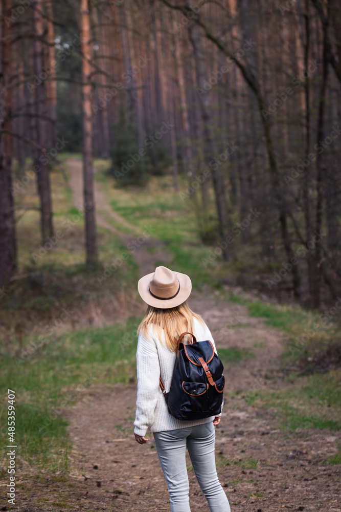 Woman with cowboy hat and backpack hiking on footpath in forest. Exploring new journey in nature