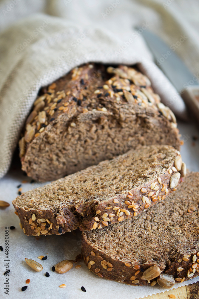 Delicious freshly baked rye bread, also called brown bread.Whole grain sliced ​​organic bread consisting of seeds on a wooden cutting board.Burlap, craft paper and a knife in the background.Close-up.