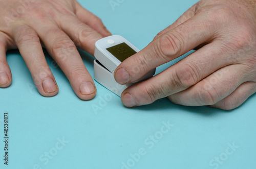 An adult male holds a pulse oximeter on his index finger.