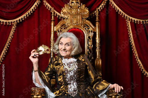Happy beautiful senior queen with mask on throne