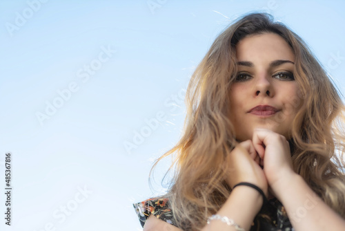 Portrait of atractive long haired young woman posing outdoors against blue sky. Bottom view.