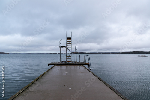 Fototapeta Naklejka Na Ścianę i Meble -  Bridge and diving tower surrounded by calm water on grey day