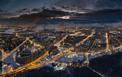 Aerial winter cityscape of St. Petersburg - Russia at dusk, drone flies over huge housing estates and public park, construction cranes, night illumination, clouds float below drone © Vladimir Drozdin