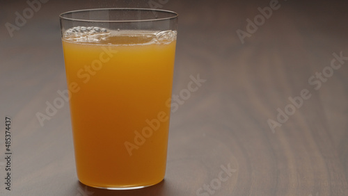 pour orange lemonade in tumbler glass on wood table with copy space