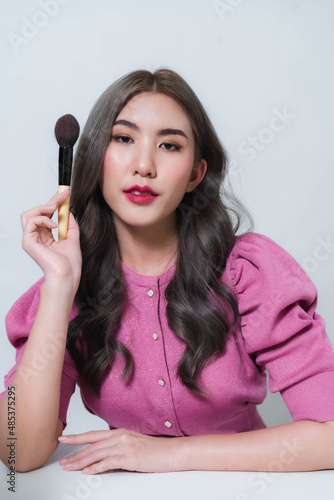 Asian woman holding a blush brush. Concept photo of a beautiful Asian makeup artist.