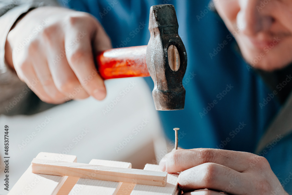 Young Caucasian carpenter in working clothes makes wooden boxes in carpentry workshop. Hands with hammer close-up. Real scene. Workflow. Small business. Environmentally friendly packaging and