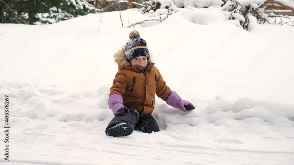 Child joyfully plays in the winter snow. Slow motion shot of little boy playing in the snowing weather, lifts with hands, blows snow up and hit her face. Cute toddler baby preschool child. Child joyfully plays in the winter snow. Slow motion shot of little boy playing in the snowing weather, lifts with hands, blows snow up and hit her face. Cute toddler baby preschool child.