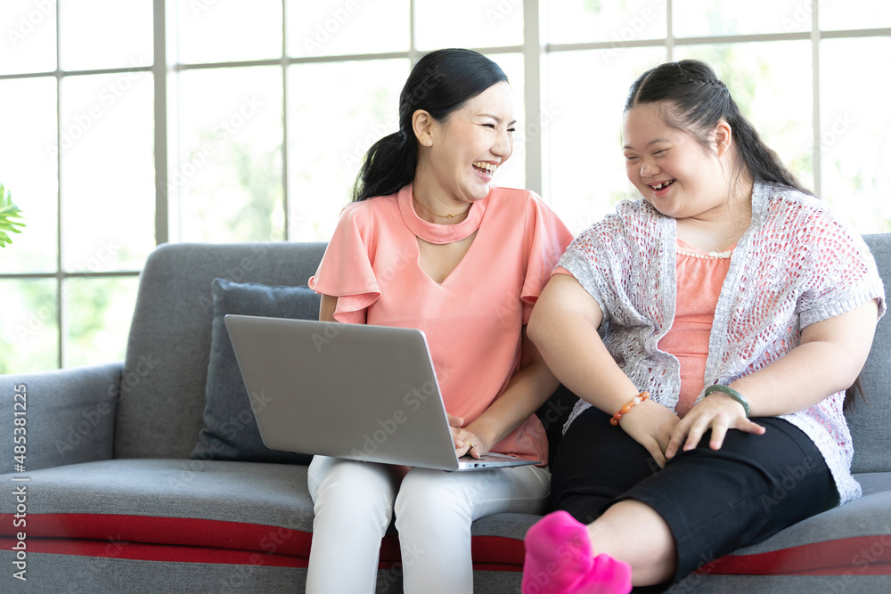 mother using laptop computer with a girl down syndrome or her daughter, smiling and enjoying on sofa