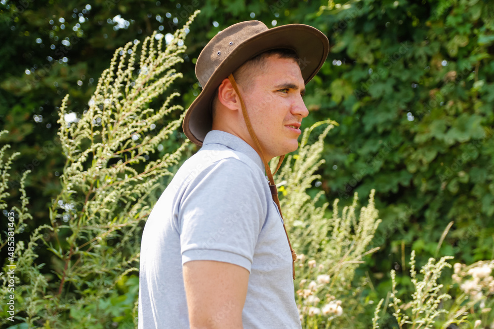 Male in hat. Portrait of smiling farmer with  green grass and trees nature in background. Young man wearing cowboy hat in field. Closeup. Happy young person. Summer male person