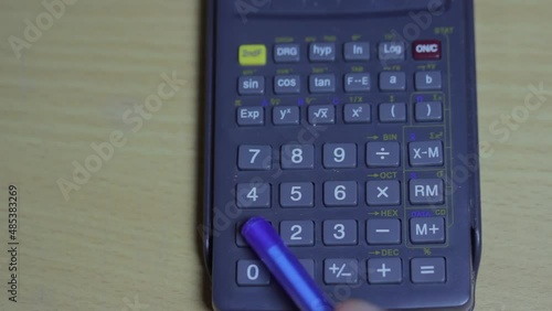 The man uses a calculator that lies on the table. He presses the buttons with his pen.