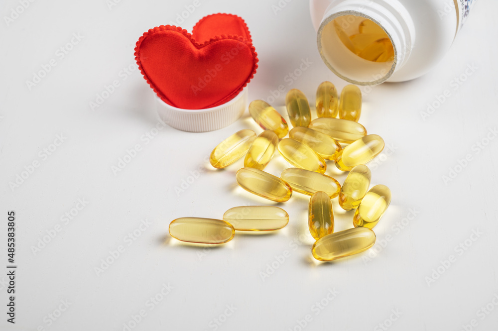 Gold fish oil isolated on white background with red hearts. Pile of fish oil with Omega 3 acid. Concept of healthy heart Gold fish oil isolated on white background with red hearts. Pile of fish oil with Omega 3 acid. Concept of healthy heart