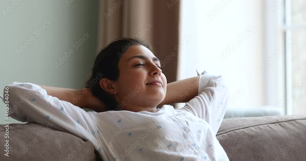 Close up attractive young Indian woman relaxing on sofa with hands behind head, enjoy healthy daytime nap alone at modern house with climate control air conditioning system. Smart home owner concept Close up attractive young Indian woman relaxing on sofa with hands behind head, enjoy healthy daytime nap alone at modern house with climate control air conditioning system. Smart home owner concept