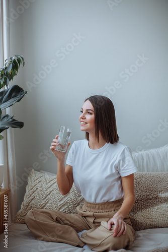 Young woman sitting on bed at home with a glass of water