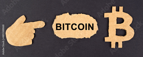 On a black background, cardboard figures of bitcoin and a hand pointing to a sign with the inscription - Bitcoin