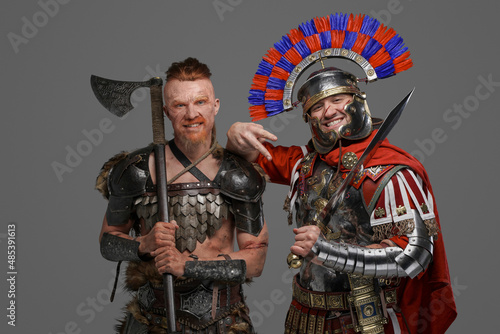 Joyful viking and roman soldier posing against gray background