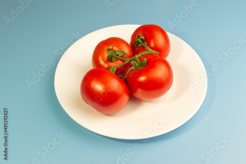 Red tomatoes on a white plate on a blue background © Екатерина Сулина