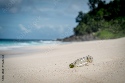 plastic rubbish washed up from ocean on sandy white beach gentle waves in paradise mountain background pollution