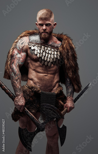 Furious viking dressed in fur and armor holding two axes