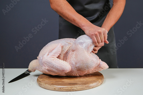 Male hands cut the carcass of a large Turkey on a wooden board. Fresh meat.