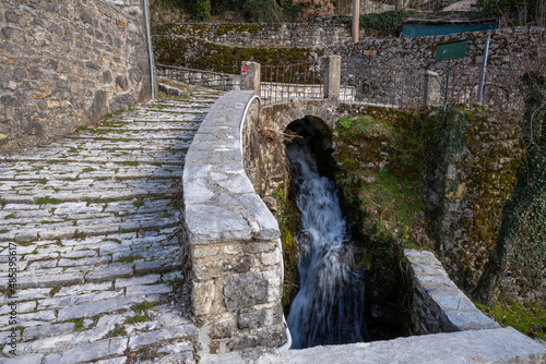 Small stream of water running by an ancient stone path Old traditional stone fountain next to a natural spring and a stone path at the traditional village of Kalarites in Tzoumerka, Greece photo