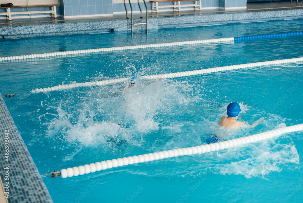 A group of boys and girls play, jump into the water in a modern pool. Development of children's sports. Healthy parenting and promotion of children's sports.