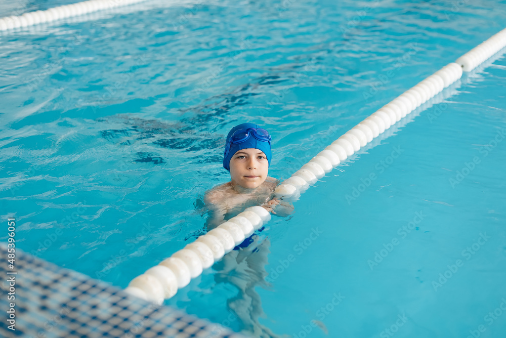 A little boy of eight years old is learning to swim in a modern swimming pool. Development of children's sports. Healthy parenting and promotion of children's sports.