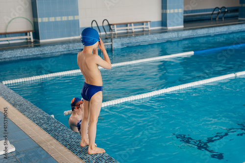 A group of boys and girls play and learn to swim in a modern swimming pool. Development of children's sports. Healthy parenting and promotion of children's sports. © Andrii