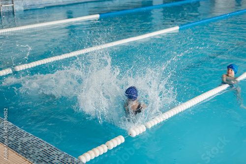 A group of boys and girls play and learn to swim in a modern swimming pool. Development of children's sports. Healthy parenting and promotion of children's sports.