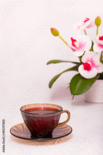 Flower tea karkade. Delicious herbal tropical drink on a bright table. A cup of pink tea from dry hibiscus petals, a natural medicinal drink against the background of fern leaves. Tropical morning.