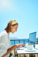 Side portrait freelancer woman using laptop computer browsing online checking messages, in wireless earphones enjoying working at terrace outdoor cafe