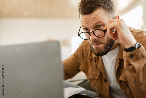 Shocked Freelancer Man Looking At Laptop Above Eyeglasses Indoor photo