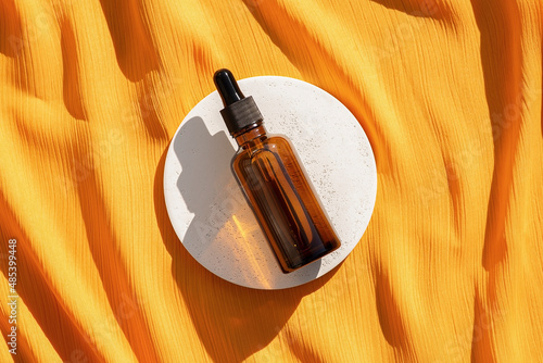 Amber glass dropper bottle with pipette on the white podium on yellow fabric background. Skincare products , natural cosmetic. Beauty concept for face and body care.
