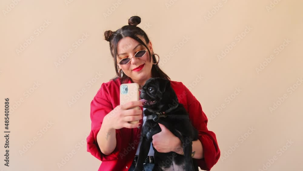Stylish trendy woman makes a selfie online life stream video call chat on mobile phone with her pet dog, a black pug. Talking over conference recording vlog. Remote communication. Stylish trendy woman makes a selfie online life stream video call chat on mobile phone with her pet dog, a black pug. Talking over conference recording vlog. Remote communication.
