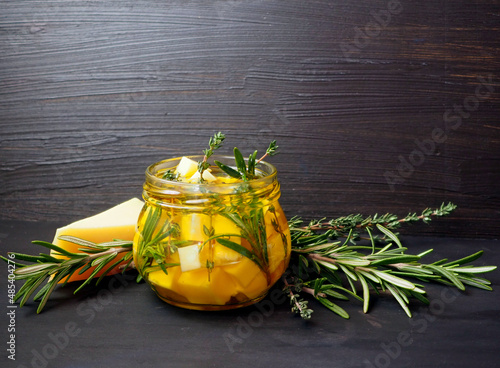Pieces of cheese with rosemary, thyme marinated in olive oil. Traditional Mediterranean snack. On a dark wooden vintage background