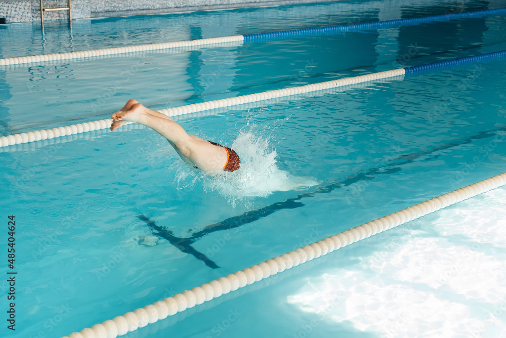 A young man dives and jumps into the water of a modern swimming pool. Training and sports development. Preparation for competitions, and a healthy lifestyle. Water treatments and a healthy lifestyle.