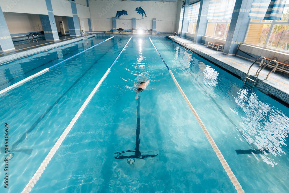 Obraz premium A young man trains and swims in a modern swimming pool. Sports development. Preparation for competitions, and a healthy lifestyle. Water treatments and a healthy lifestyle.