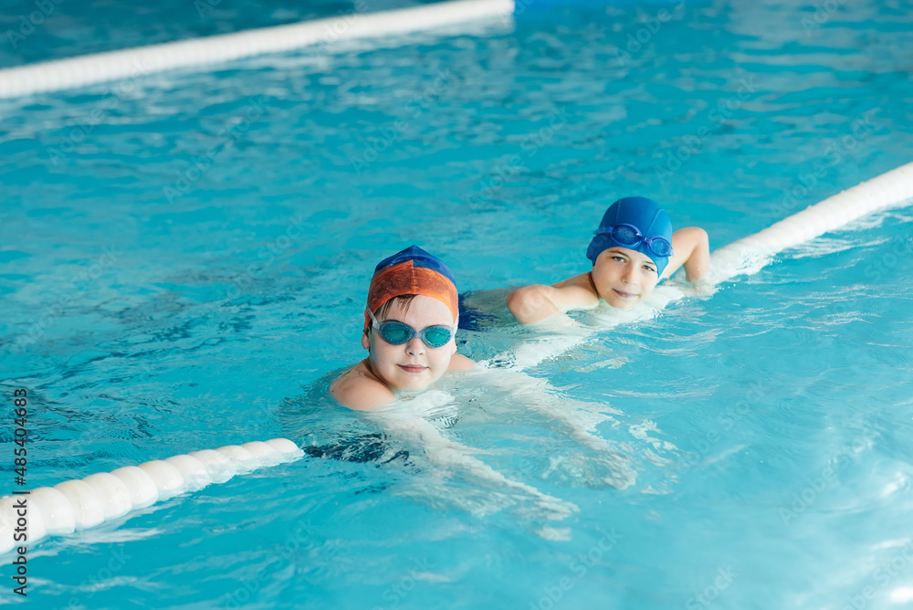 A group of boys play and learn to swim in a modern swimming pool. Development of children's sports. Healthy parenting and promotion of children's sports.
