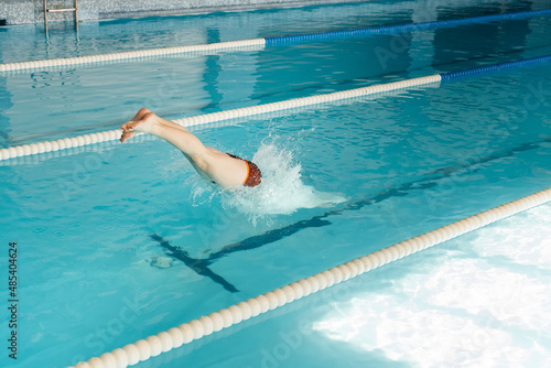A young man dives and jumps into the water of a modern swimming pool. Training and sports development. Preparation for competitions  and a healthy lifestyle. Water treatments and a healthy lifestyle.