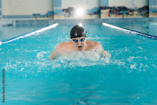 A young man trains and swims in a modern swimming pool. Sports development. Preparation for competitions, and a healthy lifestyle. Water treatments and a healthy lifestyle. © Andrii