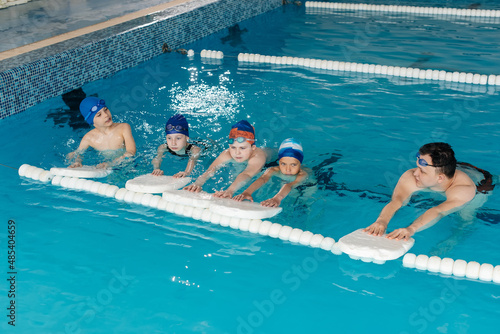 A group of boys and girls train and learn to swim in a modern swimming pool with an instructor. Development of children's sports. Healthy parenting and promotion of children's sports.