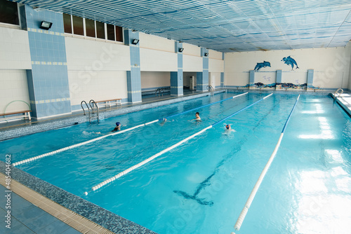 A group of boys and girls train and learn to swim in a modern swimming pool with an instructor. Development of children's sports. Healthy parenting and promotion of children's sports. © Andrii