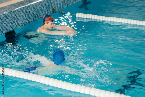 A group of boys play and learn to swim in a modern swimming pool. Development of children's sports. Healthy parenting and promotion of children's sports.