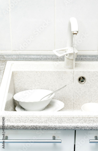 Dishwasher full of dirty dishes. Washable dishes in the sink. Dishes are ready for washing. Water flows from the tap.